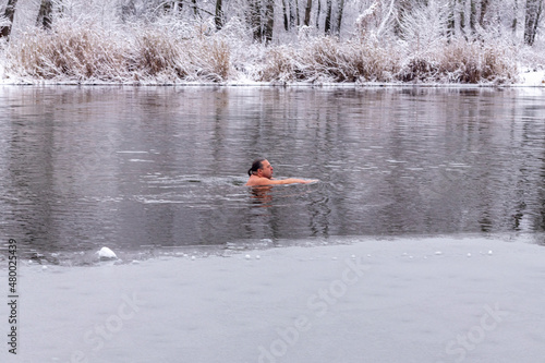 A middle-aged man swims on a cold winter day along the river against the backdrop of snow-covered trees. The concept of hardening, healthy lifestyle