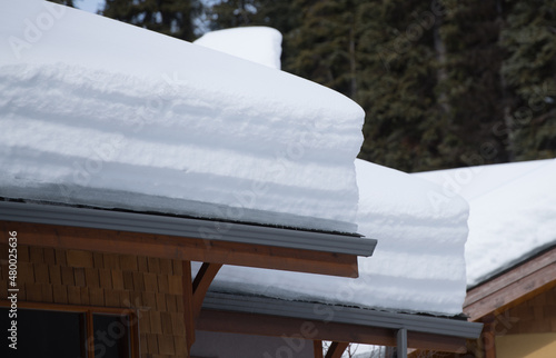 layers of snow heavy load on roof of home or ski chalet eaves or gutters of house in winter snow load on roof winter maintenance possible roof damage  horizontal format room for type photo