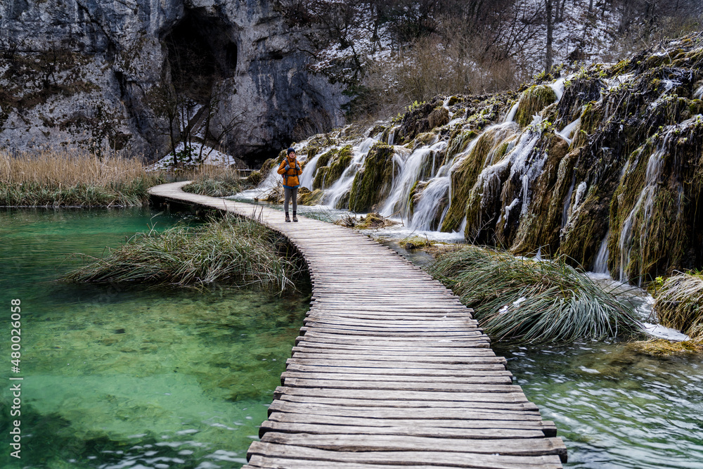 Obraz premium Women hiking rustic wooden boardwalk with small waterfalls in Plitvice Lakes National Park, Croatia