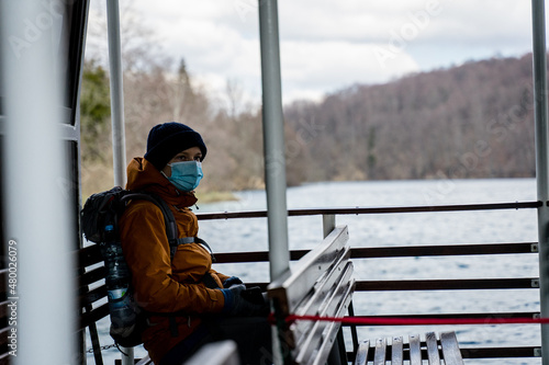 Girl, one person with yellow jacket wearing face mask and sitting in a boat in Plitvice Lakes National Park, Croatia
