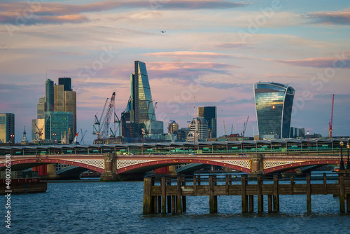 There are office buildings, skyscrapers, churches in the business against the background of blue sky and clouds, river Thames, bridge, district of London, UK.