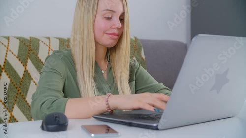 Blonde woman typing on laptop computer keyboard while working online from home on lockdown. White female with scards on face and prosthetic eye doing distant work on notebook pc connected to internet photo