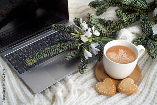 cup of cappuccino, heart-shaped cookies, laptop, spruce branches, snowdrops. romantic background, valentine's day card. congratulations on March 8. cozy scene. with love.