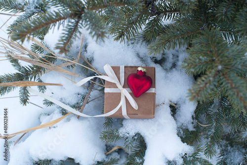 gift box and red glass heart in the snow on spruce branches. valentine's day card