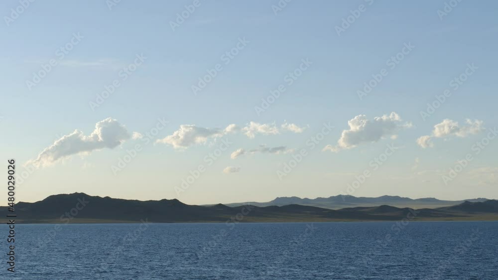 Mongolia. The lake and small waves in calm sunny weather against the background of a light blue cloudy sky. The mountains in the distance. Mongolia. The lake and small waves in calm sunny weather against the background of a light blue cloudy sky. The mountains in the distance.
