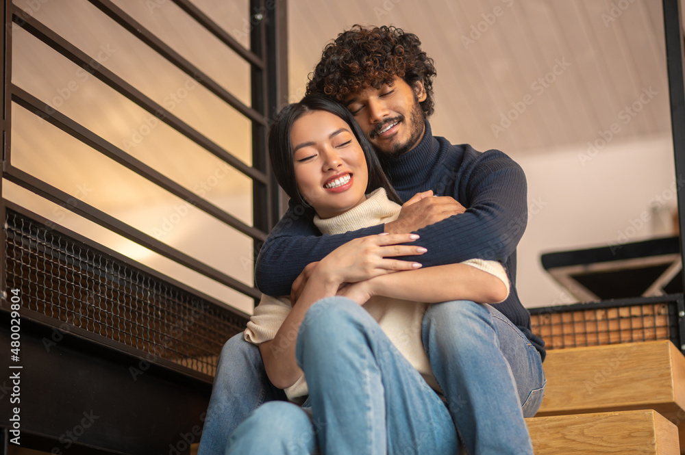 Embraced man with woman sitting on stairs at home Embraced man with woman sitting on stairs at home