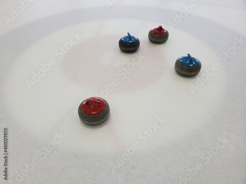 Red and blue curling stones arranged in a house on arena ice