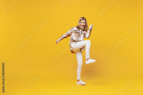 Full body smiling happy confident little blonde caucasian kid girl 13-14 years in checkered shirt hold hands crossed folded do winner gesture raise up leg isolated on plain yellow background studio