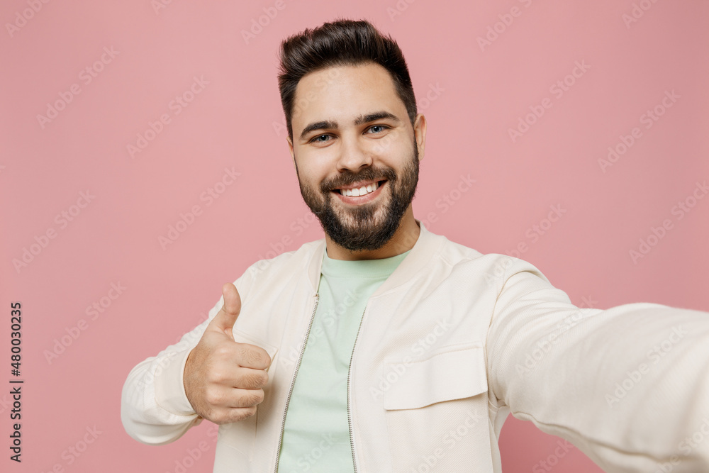 Fototapeta premium Close up young smiling happy man 20s in trendy jacket shirt doing selfie shot pov on mobile phone show thumb up gesture isolated on plain pastel light pink background studio People lifestyle concept