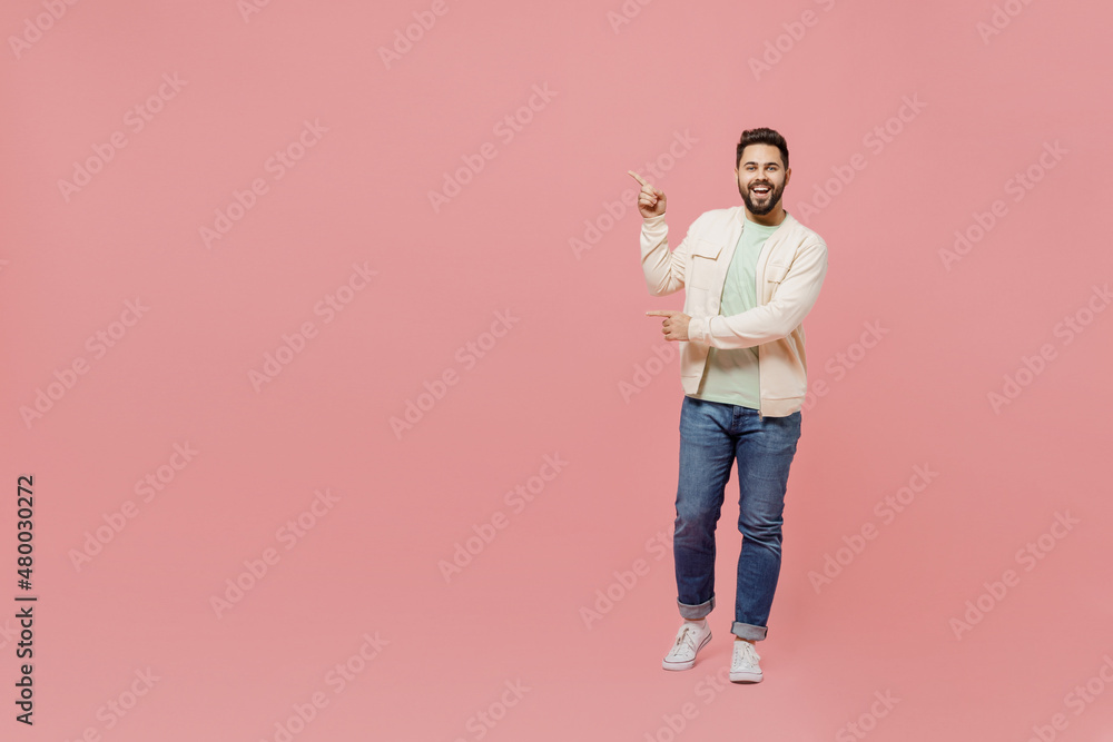 Full body young smiling happy man 20s wearing trendy jacket shirt point index fingera aside on workspace area isolated on plain pastel light pink background studio portrait. People lifestyle concept. Full body young smiling happy man 20s wearing trendy jacket shirt point index fingera aside on workspace area isolated on plain pastel light pink background studio portrait. People lifestyle concept.