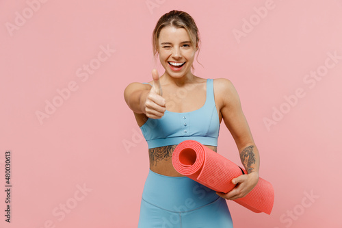 Fototapeta Naklejka Na Ścianę i Meble -  Young strong sporty athletic fitness trainer instructor woman wear blue tracksuit spend time in home gym show thumb up gesture blink isolated on pastel plain pink background. Workout sport concept