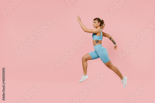 Full body young strong sporty athletic fitness trainer instructor woman wearing blue tracksuit spend time in home gym jump high isolated on pastel plain light pink background. Workout sport concept.