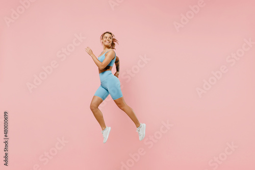 Full size young strong sporty athletic fitness trainer instructor woman wear blue tracksuit spend time in home gym jump high run isolated on pastel plain light pink background. Workout sport concept.