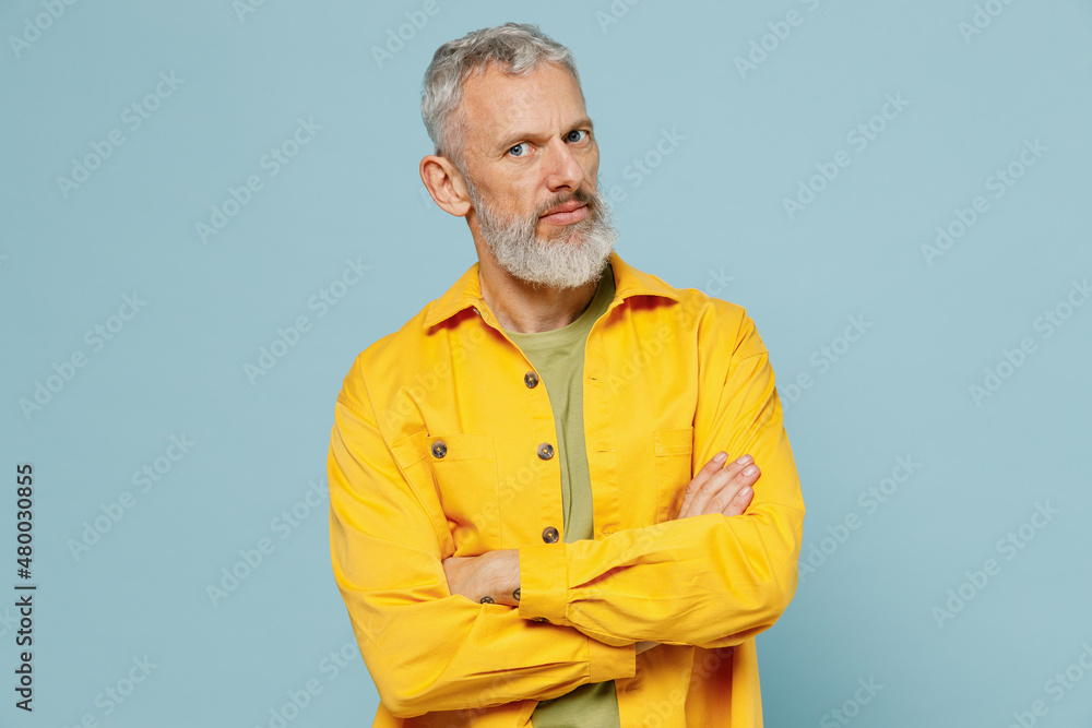Elderly calm gray-haired mustache bearded man 50s wearing yellow shirt hold hands crossed folded look camera isolated on plain pastel light blue background studio portrait. People lifestyle concept. Elderly calm gray-haired mustache bearded man 50s wearing yellow shirt hold hands crossed folded look camera isolated on plain pastel light blue background studio portrait. People lifestyle concept.