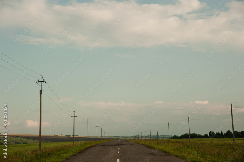 The road going beyond the horizon in the fields. Power lines along the road.