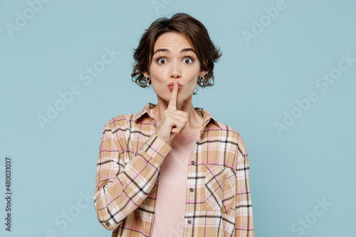 Young secret woman 20s wearing casual brown shirt says hush be quiet with finger on lips shhh gesture isolated on pastel plain light blue color background studio portrait. People lifestyle concept photo