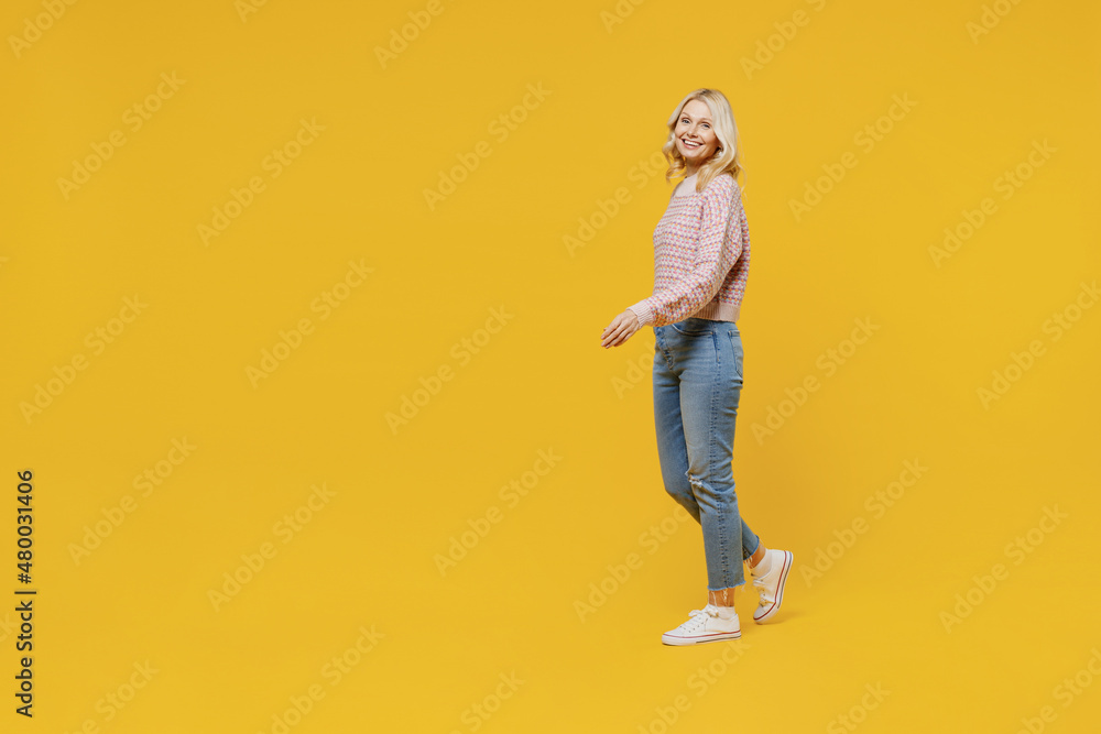 Full body side view happy fun elderly smiling blonde caucasian woman 50s in pink sweater walking going strolling isolated on plain yellow color background studio portrait. People lifestyle concept Full body side view happy fun elderly smiling blonde caucasian woman 50s in pink sweater walking going strolling isolated on plain yellow color background studio portrait. People lifestyle concept