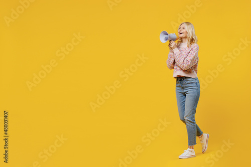 Full body elderly smiling blonde caucasian woman 50s wear pink sweater hold scream in megaphone announces discounts sale Hurry up isolated on plain yellow color background. People lifestyle concept. © ViDi Studio