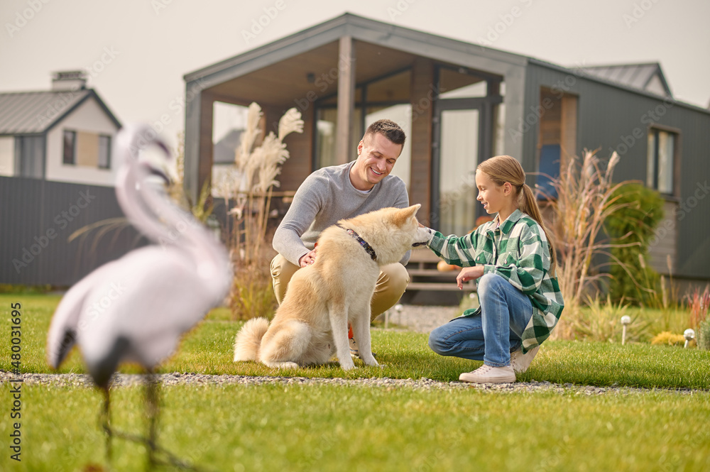 © zinkevych - Man and girl crouched near dog on lawn