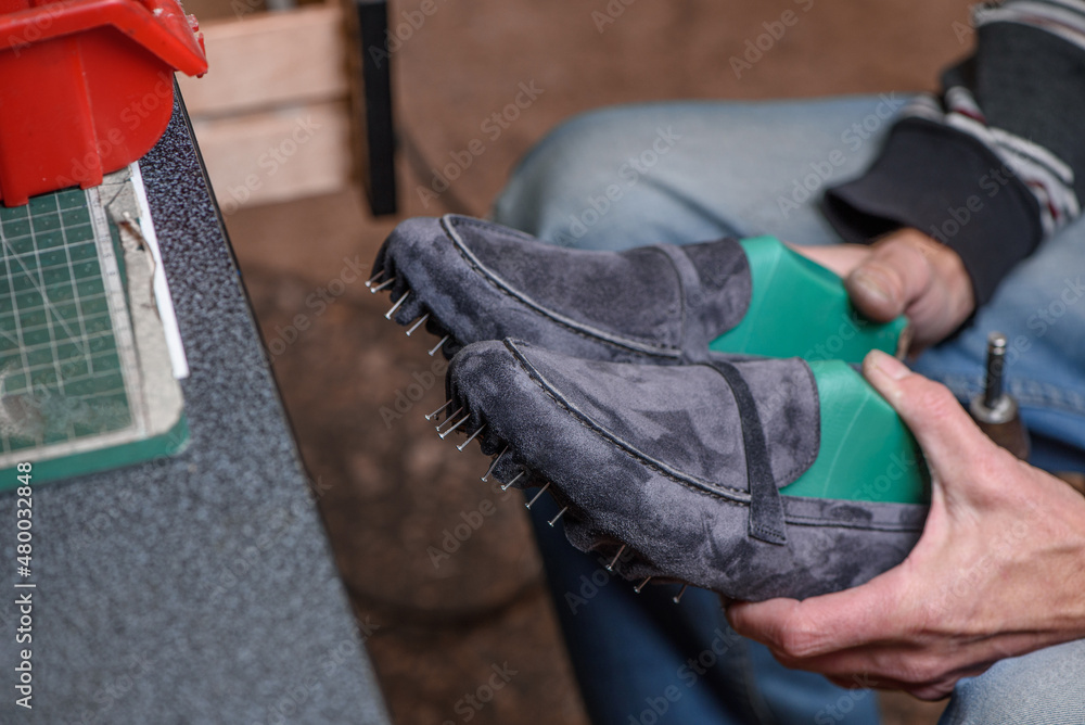 Shoemaker holding pair of new handmade suede gray shoes in his hands, checking the quality of his work. Selective focus.