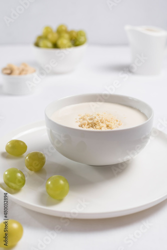 Crema de almendras, sopa fría española. Ajo blanco de Málaga con almendras y uvas en un recipiente blanco sobre una mesa blanca photo