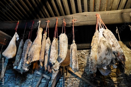 Corsican sausage specialities hanging from wooden beam in traditional stone cellar. Saucisson, coppa, lonzo, ham.