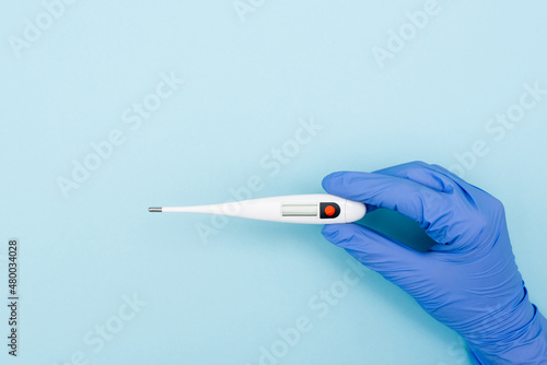 Fotografie partial view of doctor in latex glove holding electronic thermometer on blue