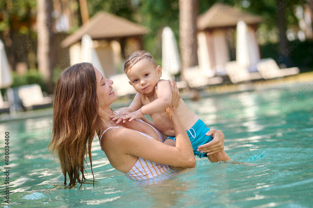 Fototapeta premium Young pretty woman in a swimming pool with her baby boy