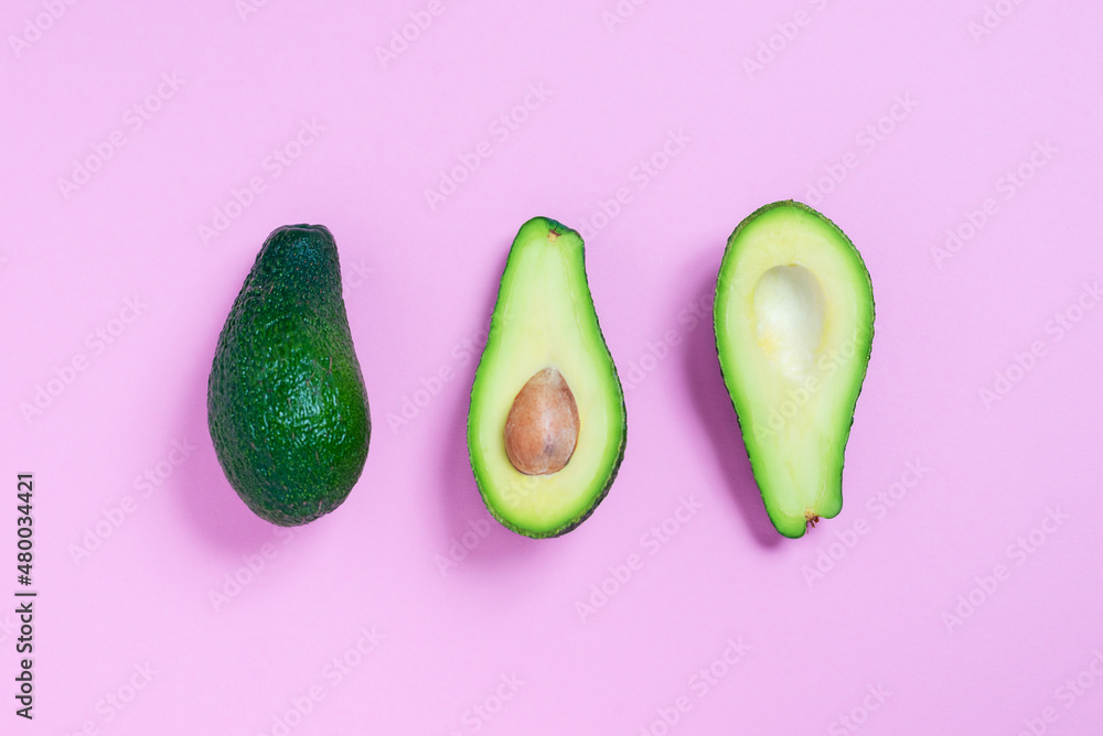 A row of halves with and without organic avocado kernels in the center of a pink background. Top view. Cooking concept