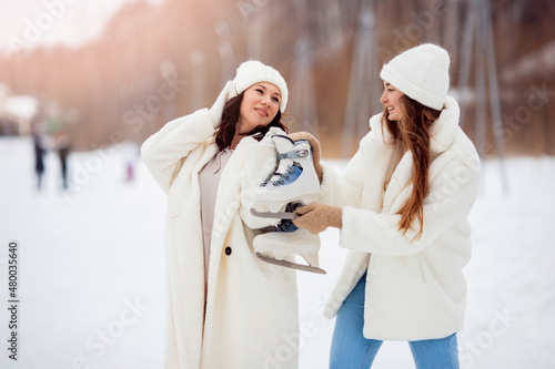 Young happy women in winter with skates on open air ice rink. Girl friendship concept