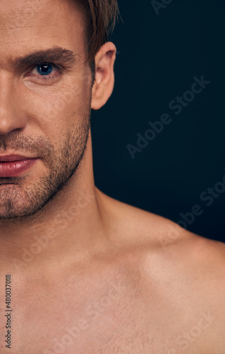 Handsome young man isolated. Cropped image of shirtless muscular man is standing on dark blue background. Half face.