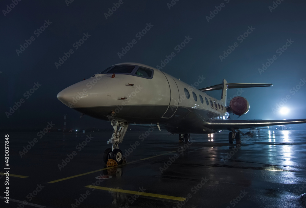 Twin-engine jet business jet parked on wet asphalt airport parking lot at night Twin-engine jet business jet parked on wet asphalt airport parking lot at night