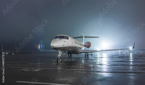 Twin-engine jet business jet parked on wet asphalt airport parking lot at night