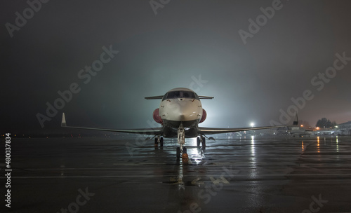 Twin-engine jet business jet parked on wet asphalt airport parking lot at night