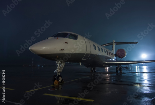 Twin-engine jet business jet parked on wet asphalt airport parking lot at night