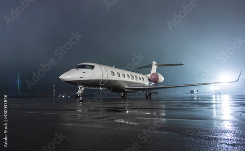 Twin-engine jet business jet parked on wet asphalt airport parking lot at night