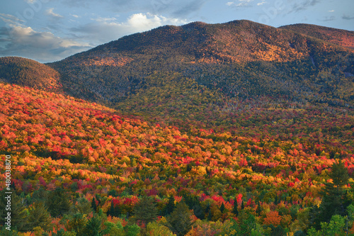 Autumn in White Mountain National Forest of New Hampshire. Late afternoon sunlight illuminating colorful hillside of fall foliage and tall peaks of north and south Twin Mountain.