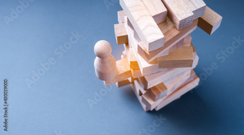 Precarious business situation concept with wooden human figurine standing on wooden block tower. photo