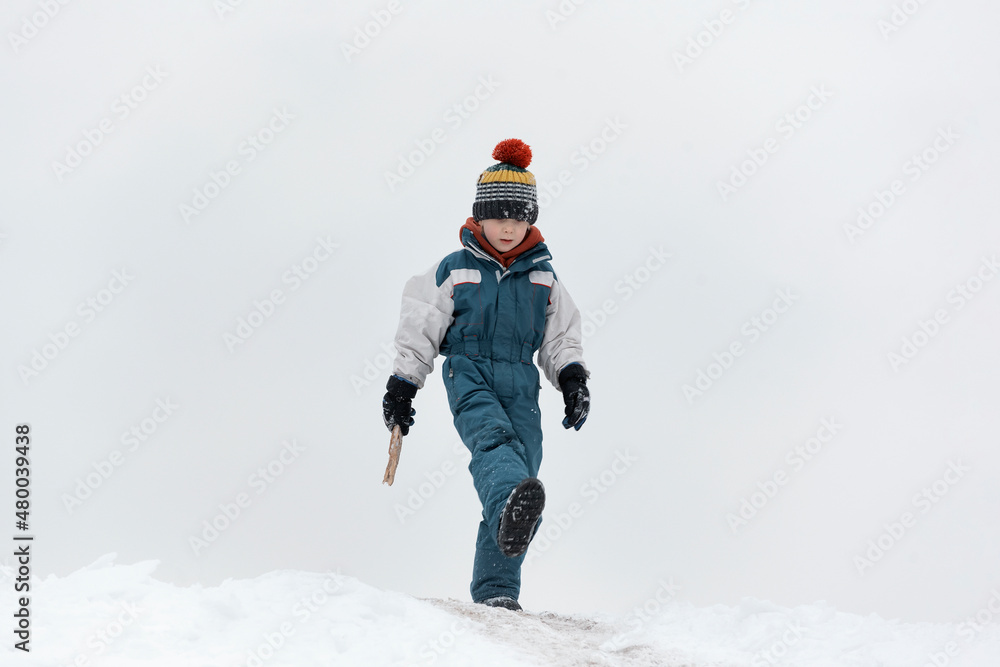 Cute boy in warm hat walking in winter Park. Child walks in the snow. Walk outside on cold winter day.