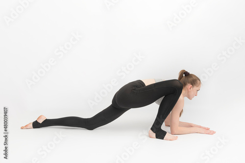 Young slender gymnast girl does an exercise to develop flexibility on white background. Asanas in yoga.