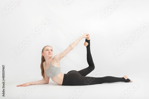 Young slender woman does yoga or gymnastics. Girl does an exercise to improve flexibility.