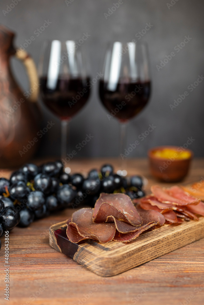 appetizer assorted meat smoked dried jamon basturma on a wooden board with grapes and wine in glasses