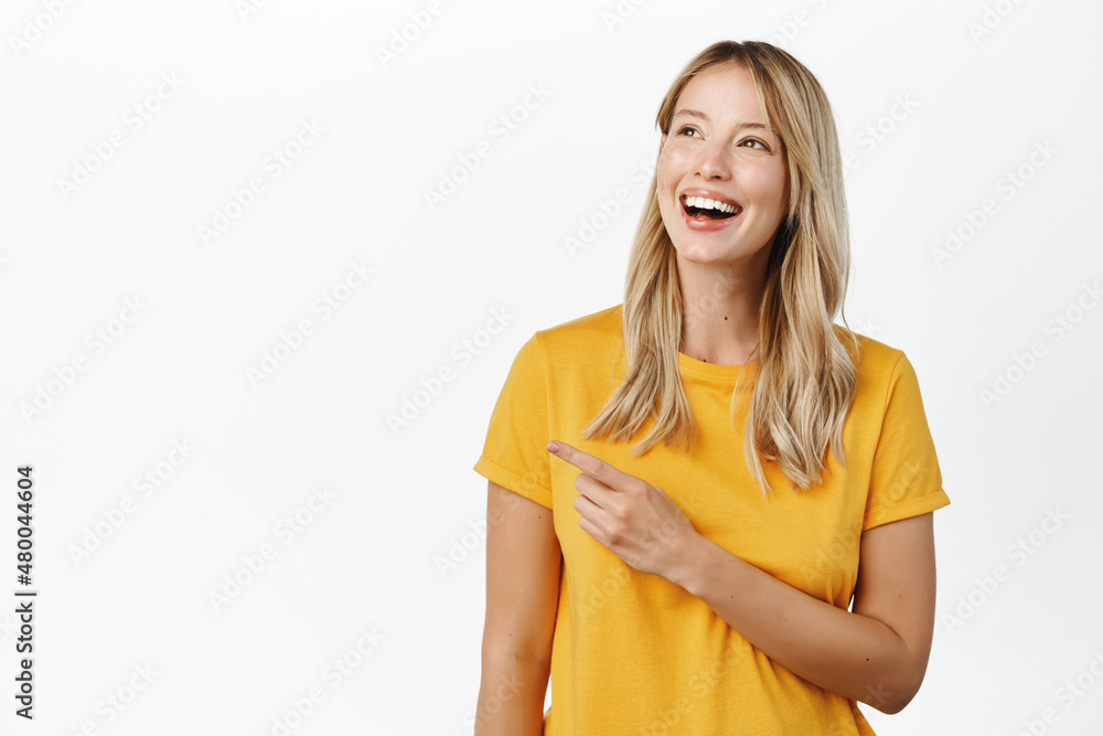 Portrait of happy smiling cute girl, woman pointing finger left at copy space, logo banner, company advertisement, standing against white background Portrait of happy smiling cute girl, woman pointing finger left at copy space, logo banner, company advertisement, standing against white background