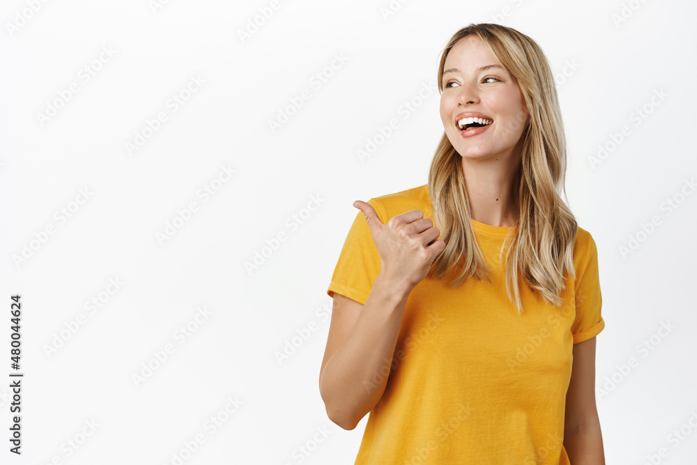 Portrait of happy smiling cute girl, woman pointing finger left at copy space, logo banner, company advertisement, standing against white background Portrait of happy smiling cute girl, woman pointing finger left at copy space, logo banner, company advertisement, standing against white background