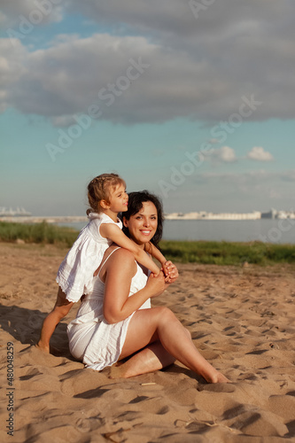mom and daughter of different nationalities play on beach in summer by sea