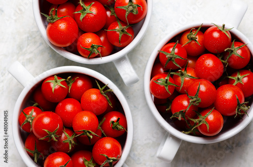 Red cherry tomatoes in white bowls on a light grey background. 