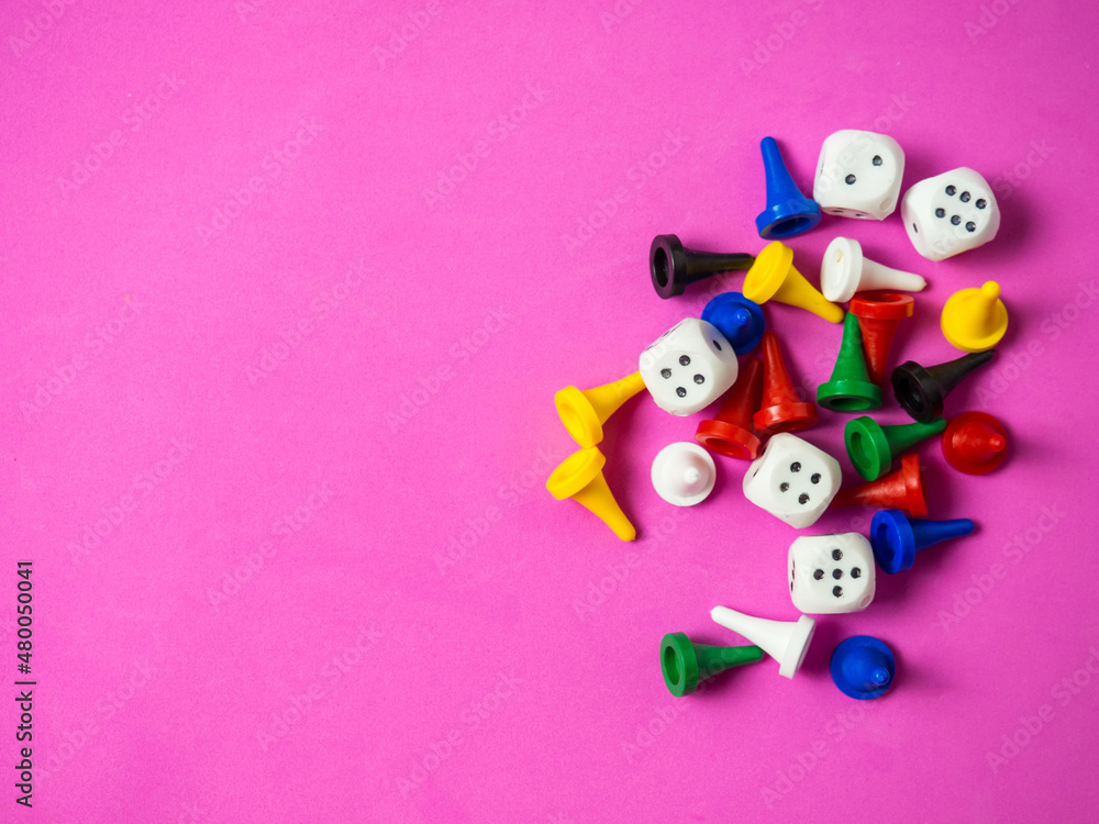 On a pink background, colorful game pieces and cubes are laid out with a place for text, games at home for the whole family, the concept of board games. On a pink background, colorful game pieces and cubes are laid out with a place for text, games at home for the whole family, the concept of board games.