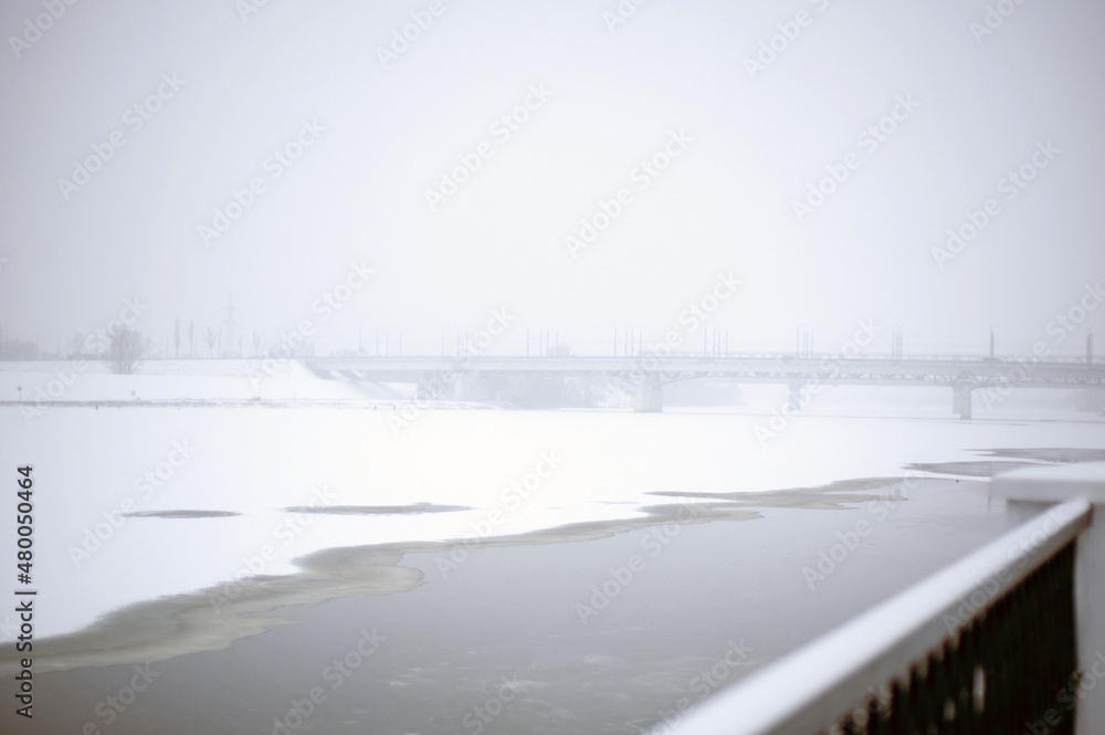 Automobile bridge over a snow-covered river in snow and fog