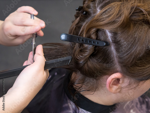 Close-up of a woman's haircut. Beautiful young brunette at the barbershop. The hairdresser is doing her hair.