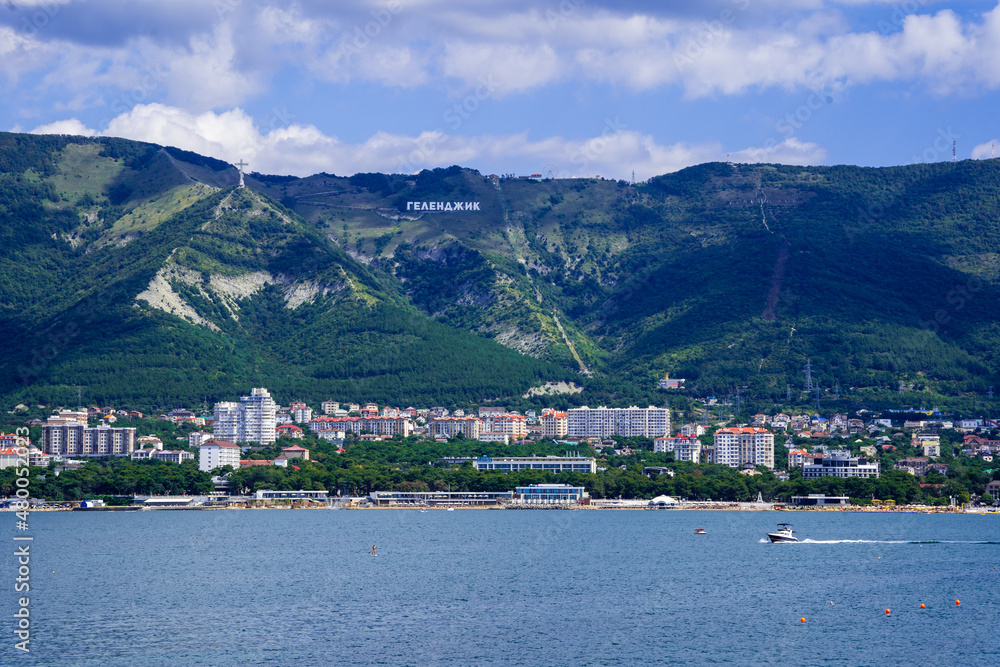 A resort town at the foot of a mountain range on the seashore. A tourist boat is traveling by sea.